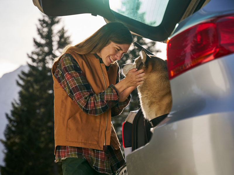 Woman stands by the luggage compartment of her VW Tiguan 1 and pets her dog