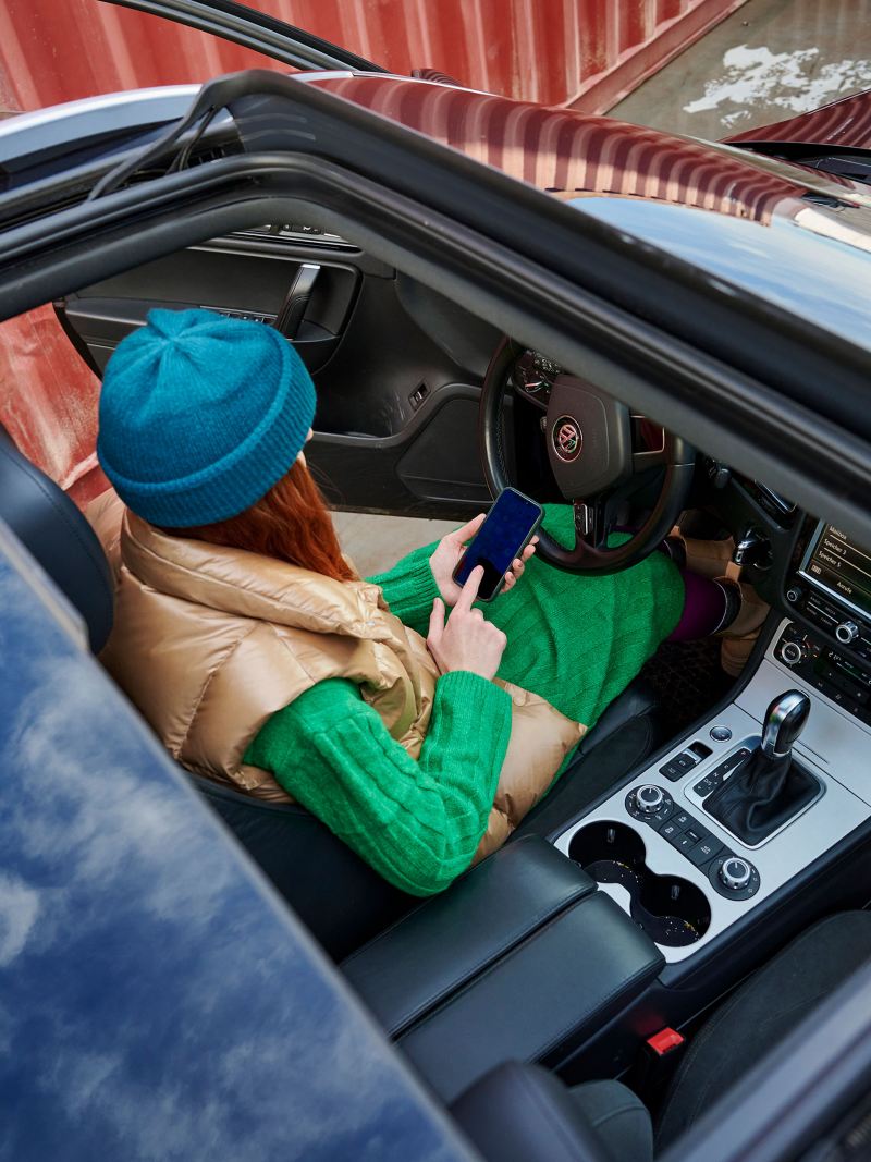運転席のドアが開いた状態で駐車中のフォルクスワーゲン トゥアレグに座ってスマートフォンを操作している女性――フォルクスワーゲンアクセサリー