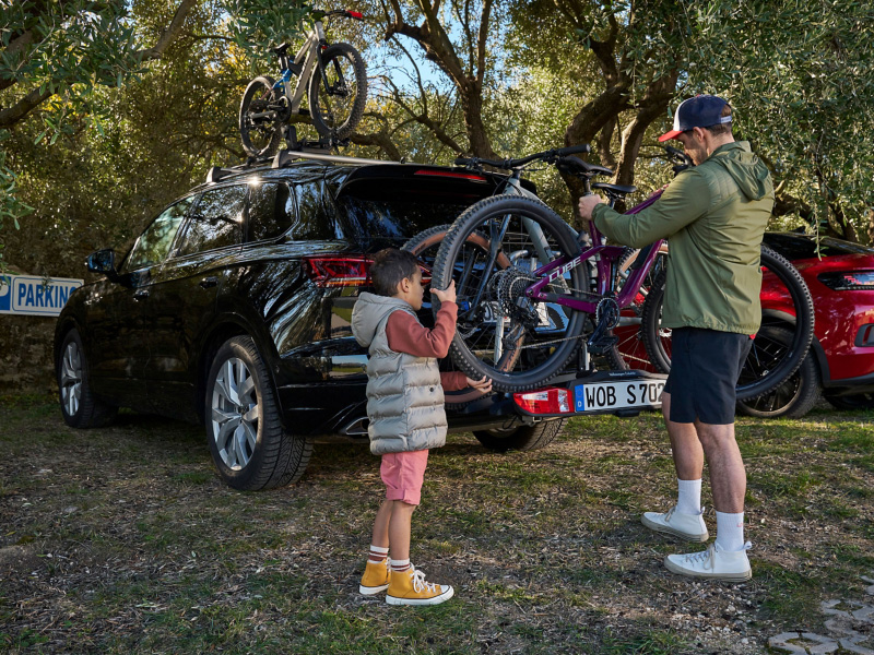 Ojciec i syn zdejmują rower z bagażnika rowerowego z oferty Akcesoriów VW, który jest zamontowany na samochodzie VW Touareg