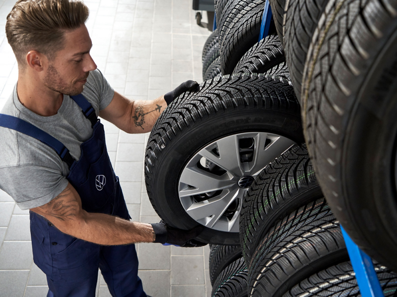Υπάλληλος Service της VW παίρνει τροχό από ένα ράφι αποθήκευσης τροχών – Υπηρεσία αποθήκευσης τροχών και ελαστικών