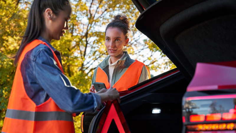 Zwei Frauen in Warnwesten stehen am Heck eines VW Elektrofahrzeugs mit geöffnetem Kofferraum.