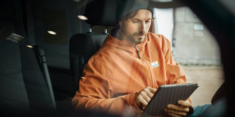 Un homme est assis dans un Transporter VW et utilise une tablette.
