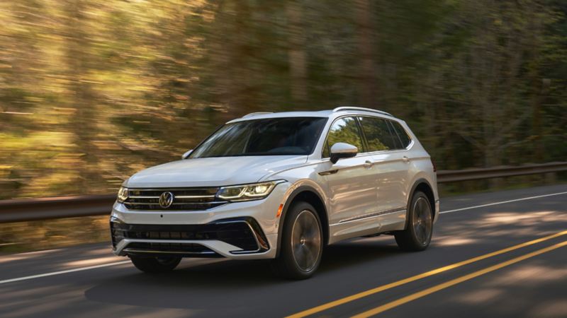 White Tiguan driving on road lined with trees 