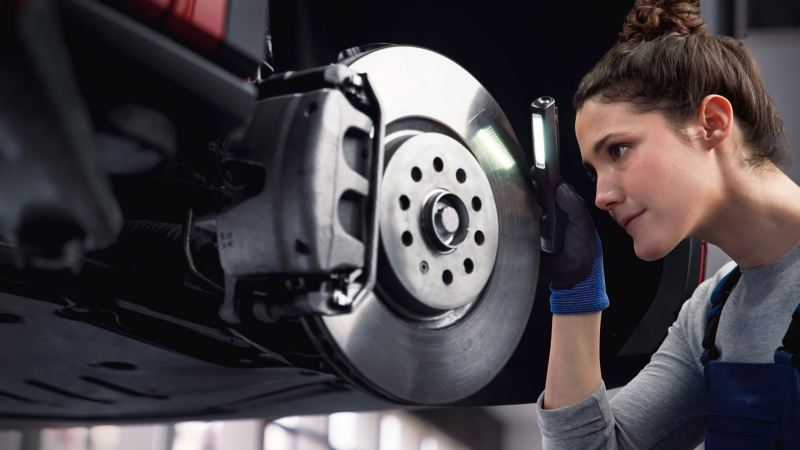 Une technicienne inspecte l'usure des disque de frein d'une voiture dans un garage