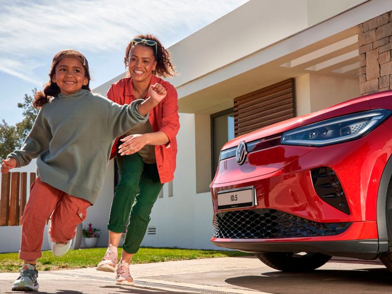 Une femme et une petite fille s'amusent à courir devant leur Volkswagen