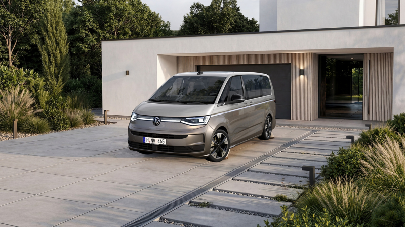 Zweifarbiger VW Multivan steht vor einer modernen Garage mit Gartenanlage