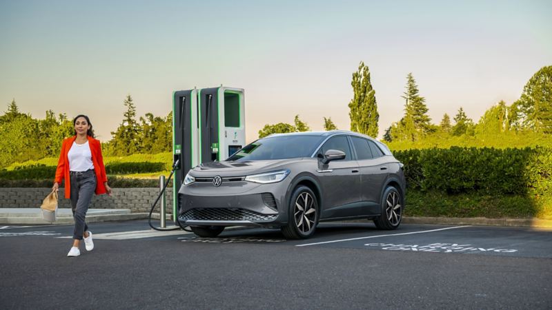 A woman walking on the street while the 2023 Volkswagen ID.4 is parked on the electric charging station.