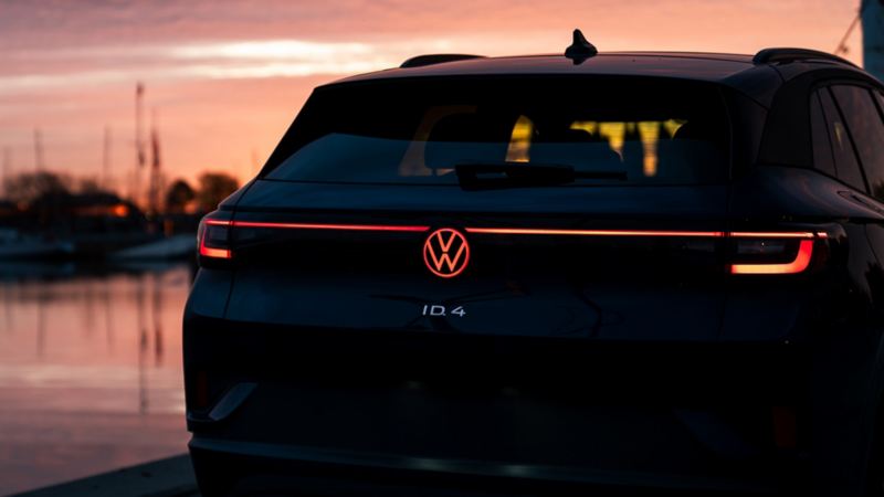 Une photo en gros plan de la Volkswagen ID.4 2024 garée pendant un coucher de soleil avec une bande lumineuse rouge à DEL intégrée