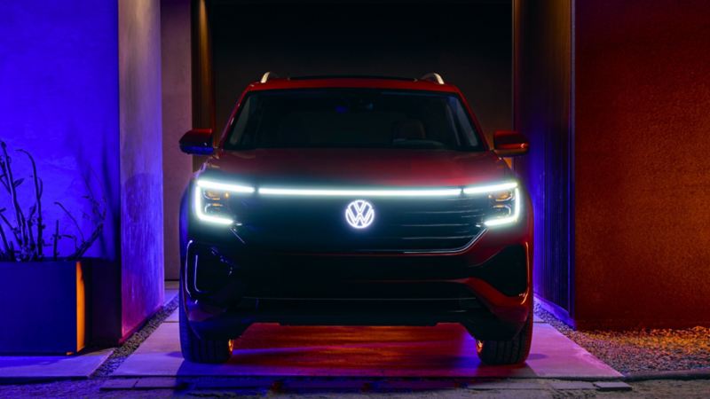 The red 2024 Volkswagen Atlas parked near a house at night with headlights turned on