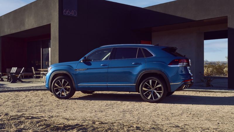 Vue arrière d’un Atlas Cross Sport 2024 de Volkswagen bleu stationné derrière une maison