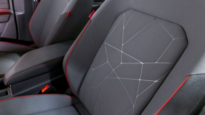 Interior of the Jetta GLI 2024. The image shows the front driver and passenger seat. The seats are black with red stitching and have a geometric pattern on the headrests.