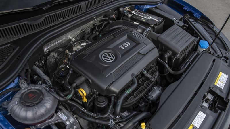 Jetta GLI 2024 engine bay. The engine is a 1.5L TSI engine with a black plastic cover with the Volkswagen logo on it. The engine bay is clean and well-maintained with various wires and hoses visible.