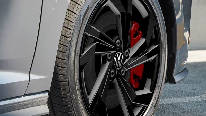 Jetta GLI 2024 wheel on the concrete surface background. The wheel is black with a silver rim and a red brake caliper. The tire is low profile.