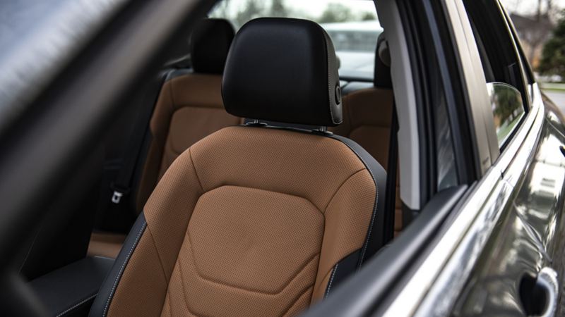 L’intérieur de la Jetta 2024 de Volkswagen, en particulier le siège passager. Le siège est de couleur beige avec un appuie-tête noir. Le siège est en cuir et a un motif perforé dessus. Le siège est en position verticale et l’appuie-tête est réglable.