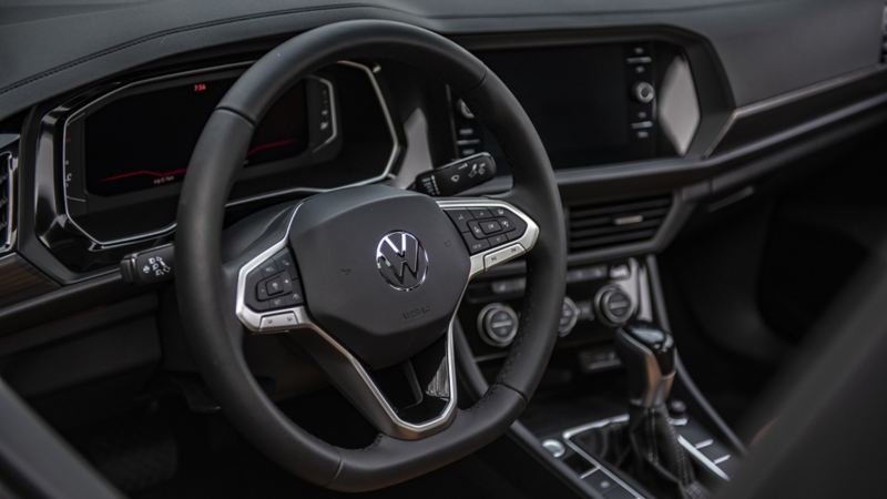 Photo de la Jetta 2024 de Volkswagen présentant son volant et son tableau de bord. Le volant est noir avec un logo Volkswagen argenté au centre. Le tableau de bord est noir avec un écran tactile au centre.