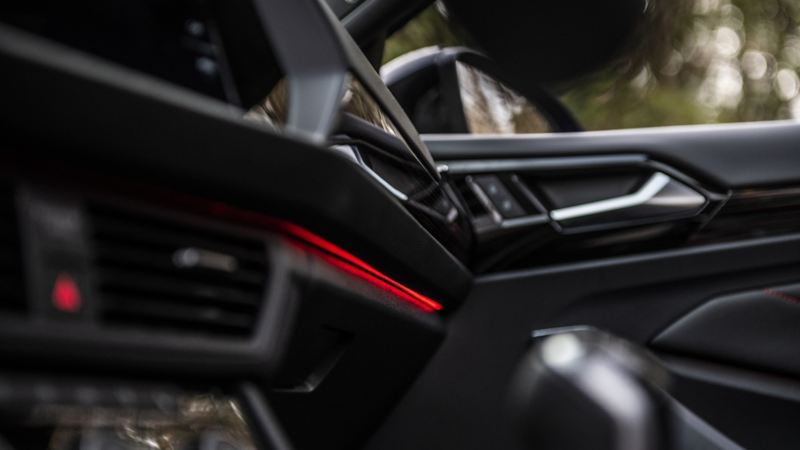 Photo de la Jetta 2024 de Volkswagen montrant l’intérieur de la voiture à partir du siège du passager. Le tableau de bord est noir avec une illumination rouge. La console centrale est aussi noire avec illumination rouge.