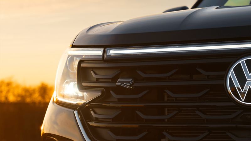 A close-up view of the Volkswagen Atlas 2025's front grille and headlights against a backdrop of a vibrant sunset sky.