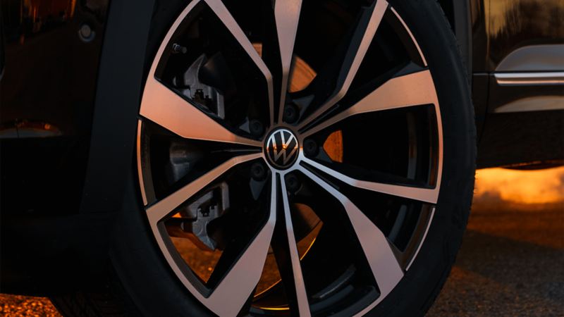 A close-up of a 2025 Atlas wheel showcases its five-spoke design with alternating black and silver sections, prominently displaying the Volkswagen logo in the centre.