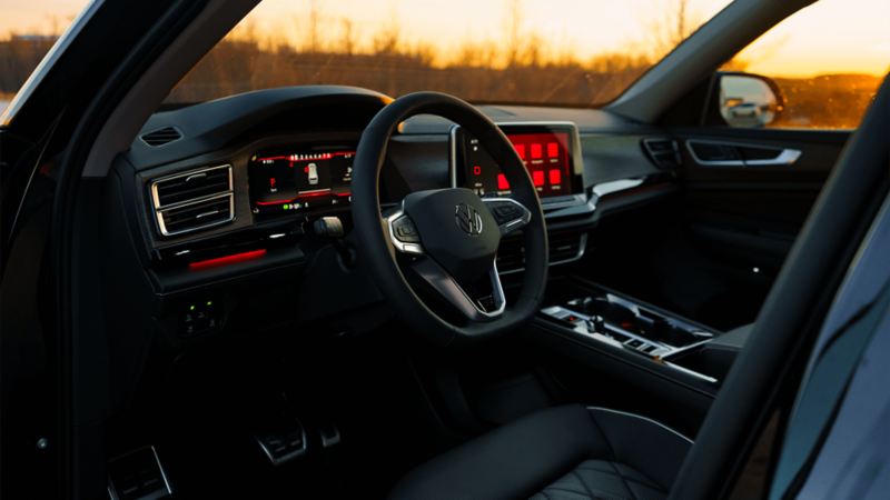 The illuminated dashboard, infotainment system, and sleek black design of the console and seats create a modern and comfortable interior view of the Atlas 2025 against a backdrop of dusk.