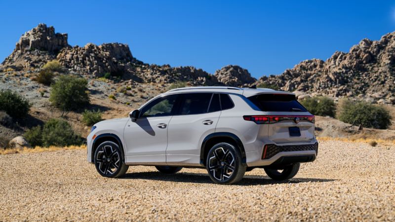 Vue latérale de le Volkswagen Tiguan 2025 blanc stationnée sur une route pittoresque avec des collines en arrière-plan.