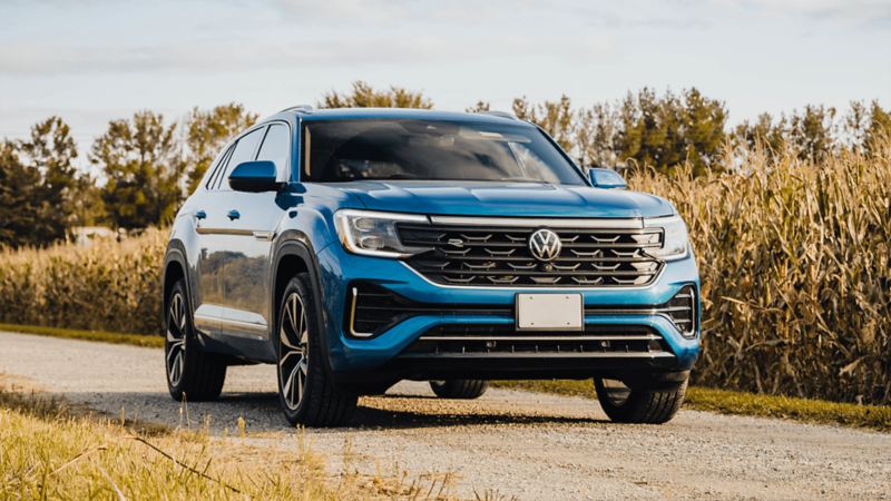 A blue Atlas Cross Sport 2025 is parked on a road with grassy fields in the background.