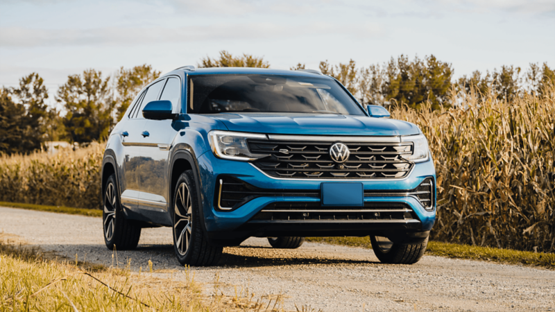 A blue Atlas Cross Sport 2025 is parked on a road with grassy fields in the background.