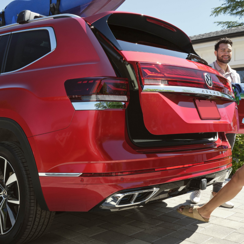 A couple loading equipment into a red 2025 Atlas with a hands-free power liftgate for easy access.
