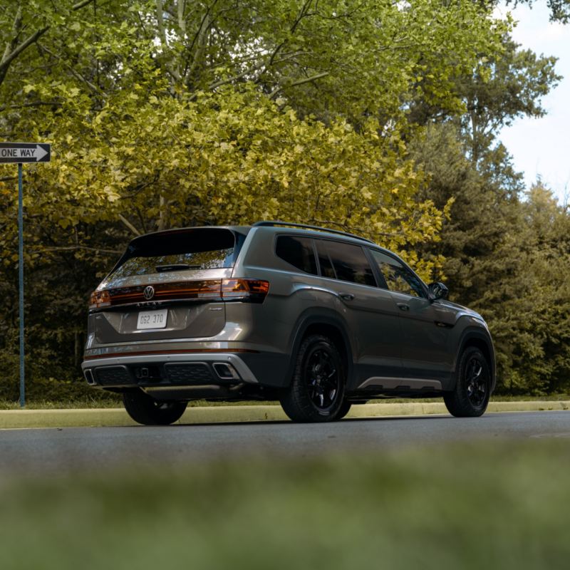 A rear view of a grey Atlas 2025, with blacked-out windows and wheels, which stands out against natural surroundings.