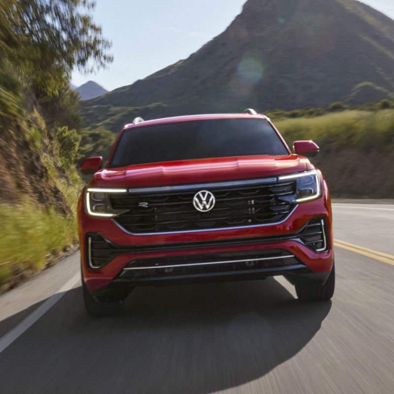 A red Volkswagen Atlas 2025 SUV cruises along a scenic mountain road.