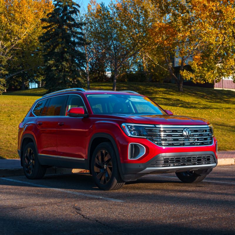 A red VW Atlas 2025 parked on the side of a road lined with lush green trees and grass.