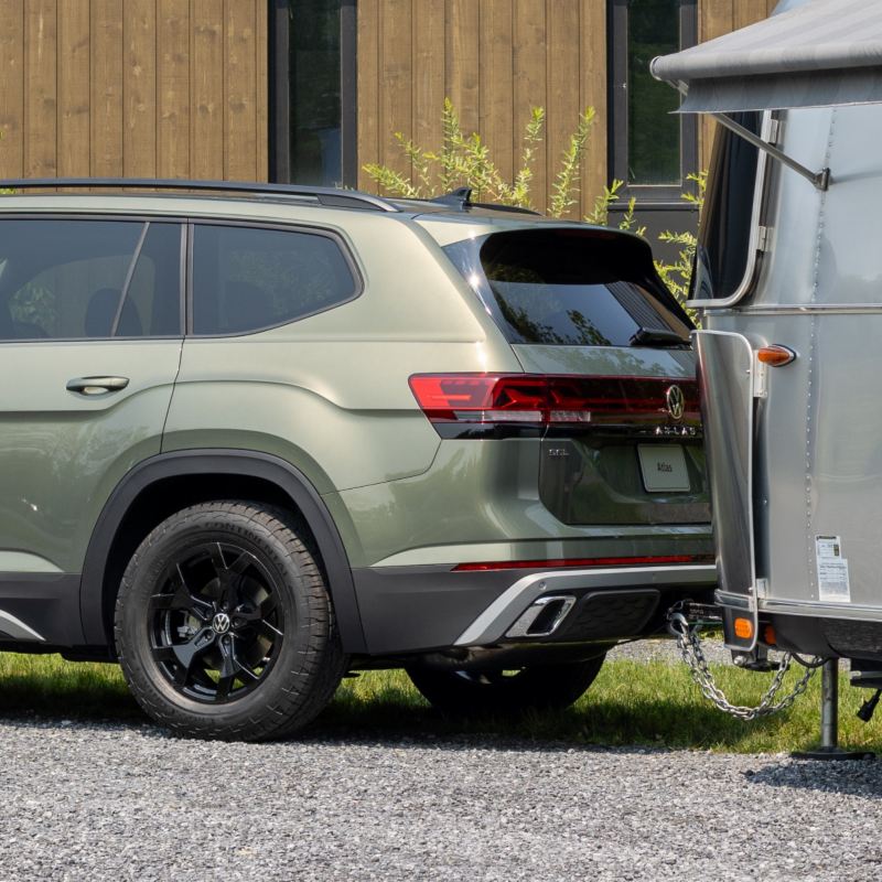 A 2025 Volkswagen Atlas parked next to a camper trailer, showcasing its standard tow hitch capable of hauling up to 5,000 pounds.