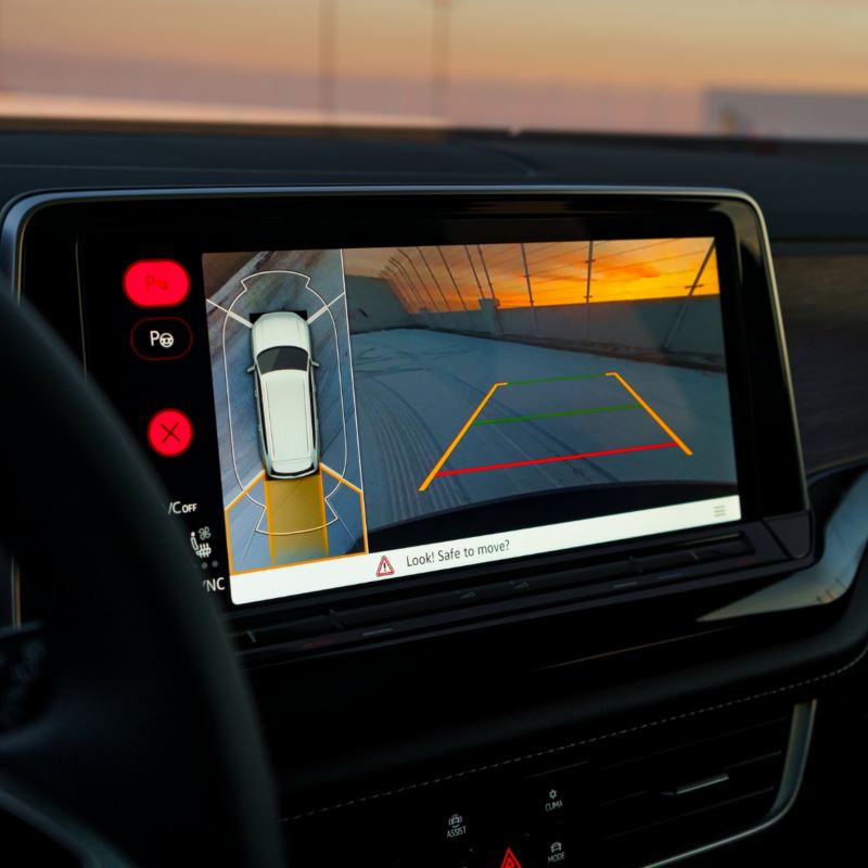 A car's infotainment system displays a 360° area view with parking guidelines, showcasing the feature against a sunset backdrop.