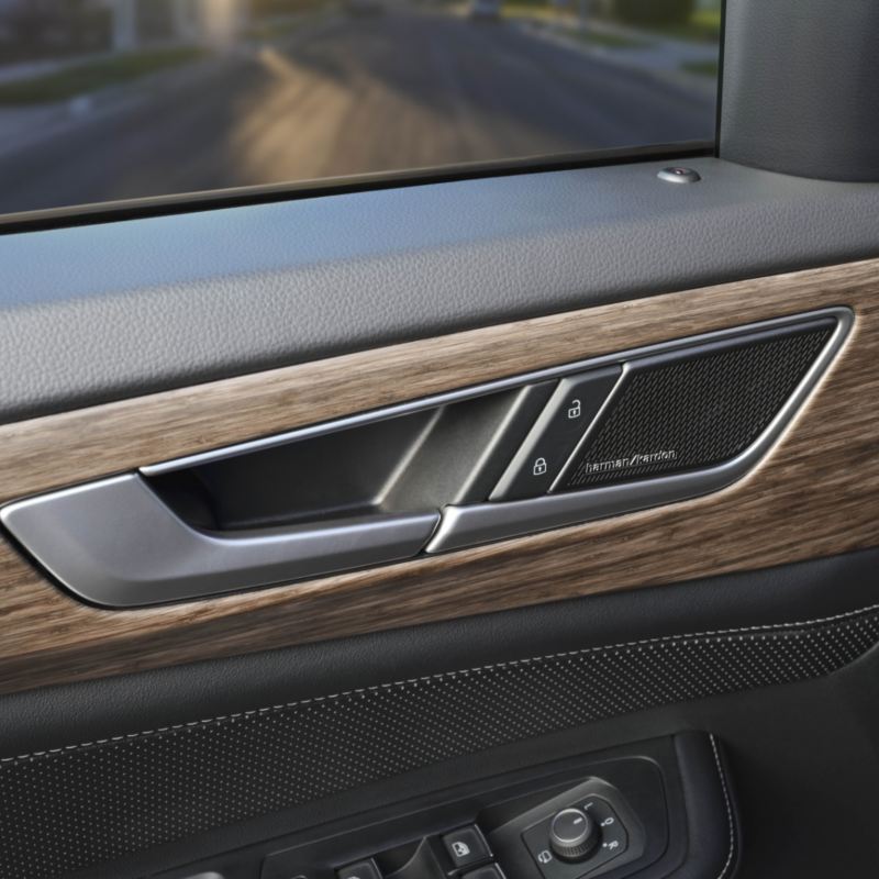 A close-up view of a Harman Kardon Premium Audio speaker system seamlessly integrated into the door panel of an Atlas 2025. The speaker grille features a metallic finish set against a stylish wood grain trim.