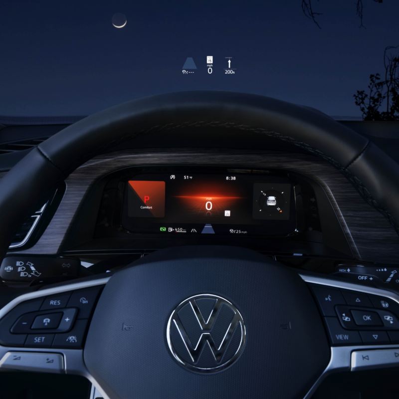 The Atlas 2025's Head-Up Display (HUD) projects key driving information onto the windshield, including a digital speedometer reading 0 km/h, navigation arrows, and other essential symbols against a backdrop of twilight sky with a crescent moon.