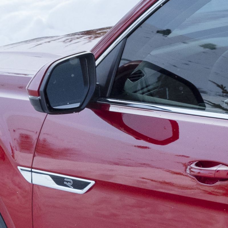 A red VW Atlas 2025 showcases its exterior mirror, equipped with heated, power-autofolding, memory, and reverse tilt-down features.