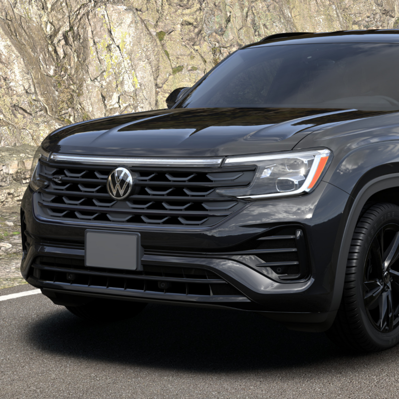 Un Volkswagen Atlas Cross Sport 2025 noir roule sur une route avec une colline rocheuse en arrière-plan.