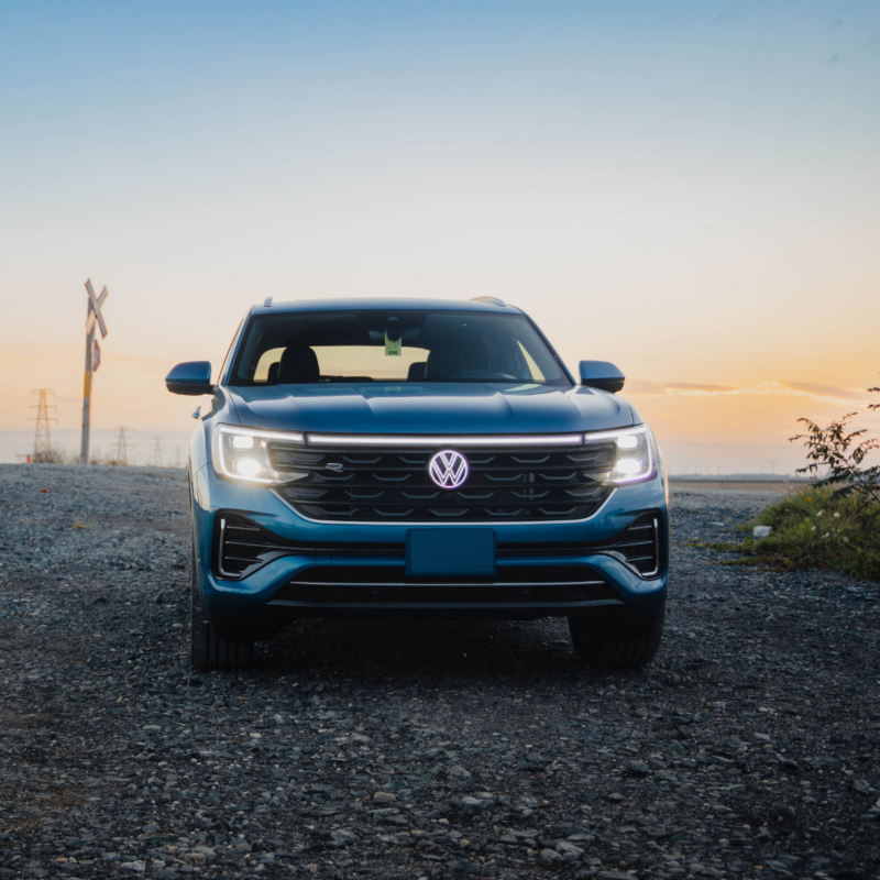 Un Atlas Cross Sport 2025 bleu est garé sur une route avec un coucher de soleil en arrière-plan, mettant en valeur ses phares.