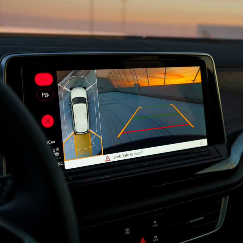 Le système d'infodivertissement de l'Atlas Cross Sport 2025 affiche une vue panoramique à 360° avec des lignes de guidage pour le stationnement, mettant en valeur cette fonctionnalité sur fond de coucher de soleil.
