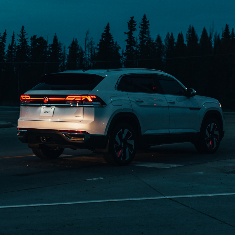 Un Atlas Cross Sport blanc est stationné sur une route forestière à la tombée de la nuit, ses feux arrière allumés.