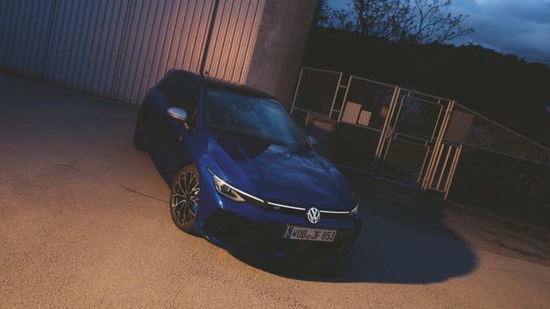 Une Volkswagen Golf R bleue équipée de freins haute performance, garée devant un grand bâtiment au crépuscule.