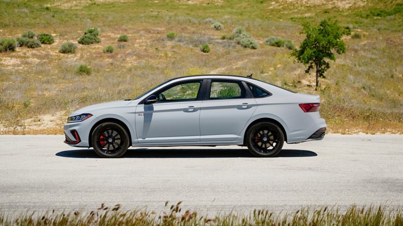 A white Jetta GLI 2025 parked outdoors with grassy hills in the background.