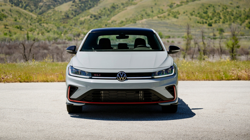 Front view of a white Jetta GLI 2025 parked outdoors with grassy hills in the background.