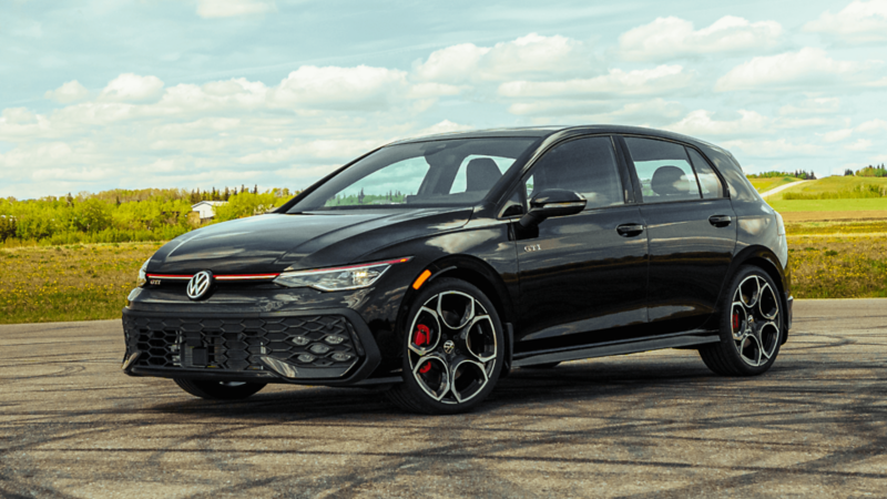 Volkswagen Golf GTI 2026 noire stationnée sur une surface pavée, avec des collines herbeuses et un ciel nuageux en arrière-plan.