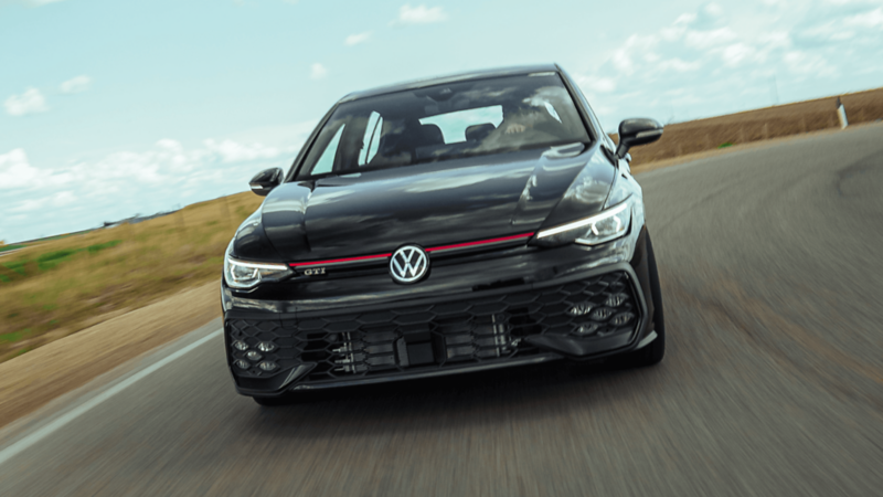Vue avant d’une Volkswagen Golf GTI 2026 noire en mouvement sur une route sinueuse, illustrant son design dynamique et ses phares à DEL.