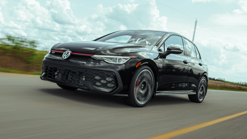 Volkswagen Golf GTI 2026 noire roulant sur une route dégagée sous un ciel nuageux.