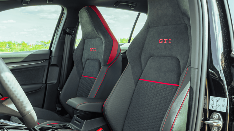 Front sport seats of the 2026 Volkswagen Golf GTI with GTI stitching, red accents, and honeycomb texture. 