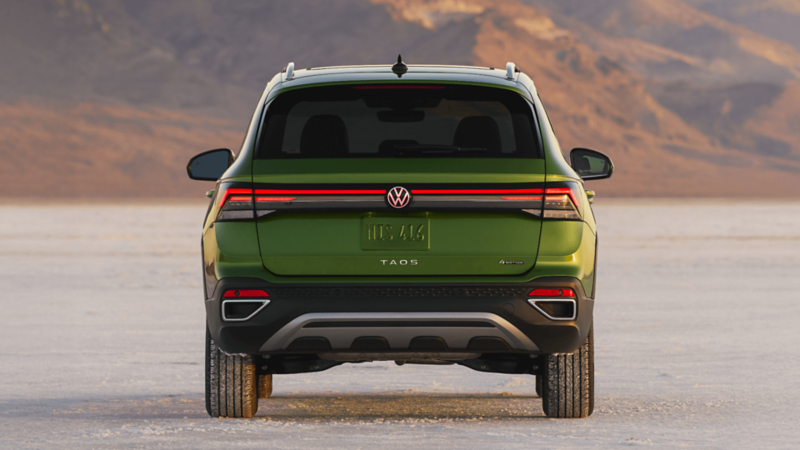 Rear view of a green 2026 Volkswagen Taos parked on a dirt road overlooking a mountainous landscape.