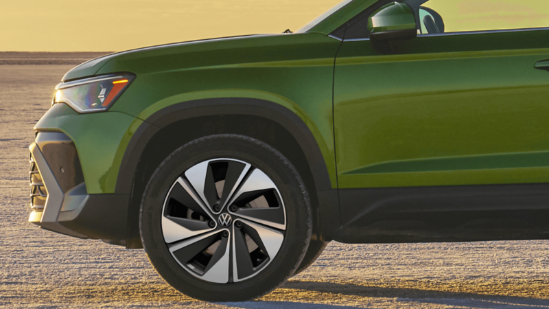 Side view of a green 2026 Taos with a sunset on the horizon