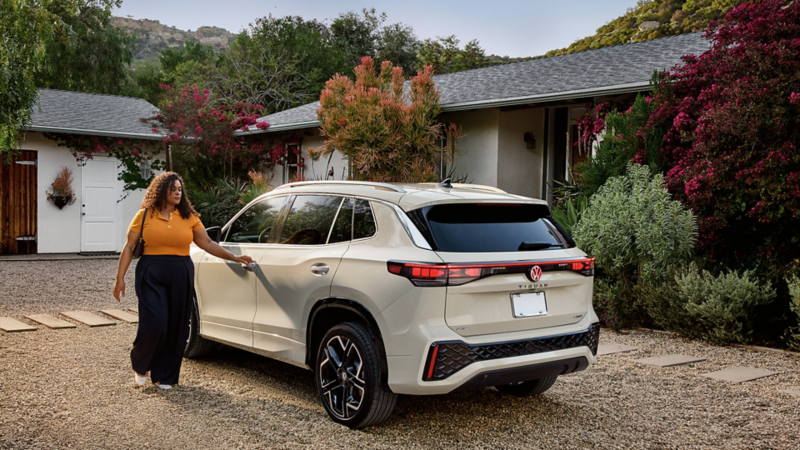 Rear view of the 2026 Volkswagen Tiguan SUV in white with a woman opening the driver’s door.