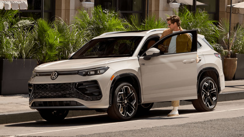 2026 Volkswagen Tiguan SUV in white with a person holding the open driver’s door in an urban setting.